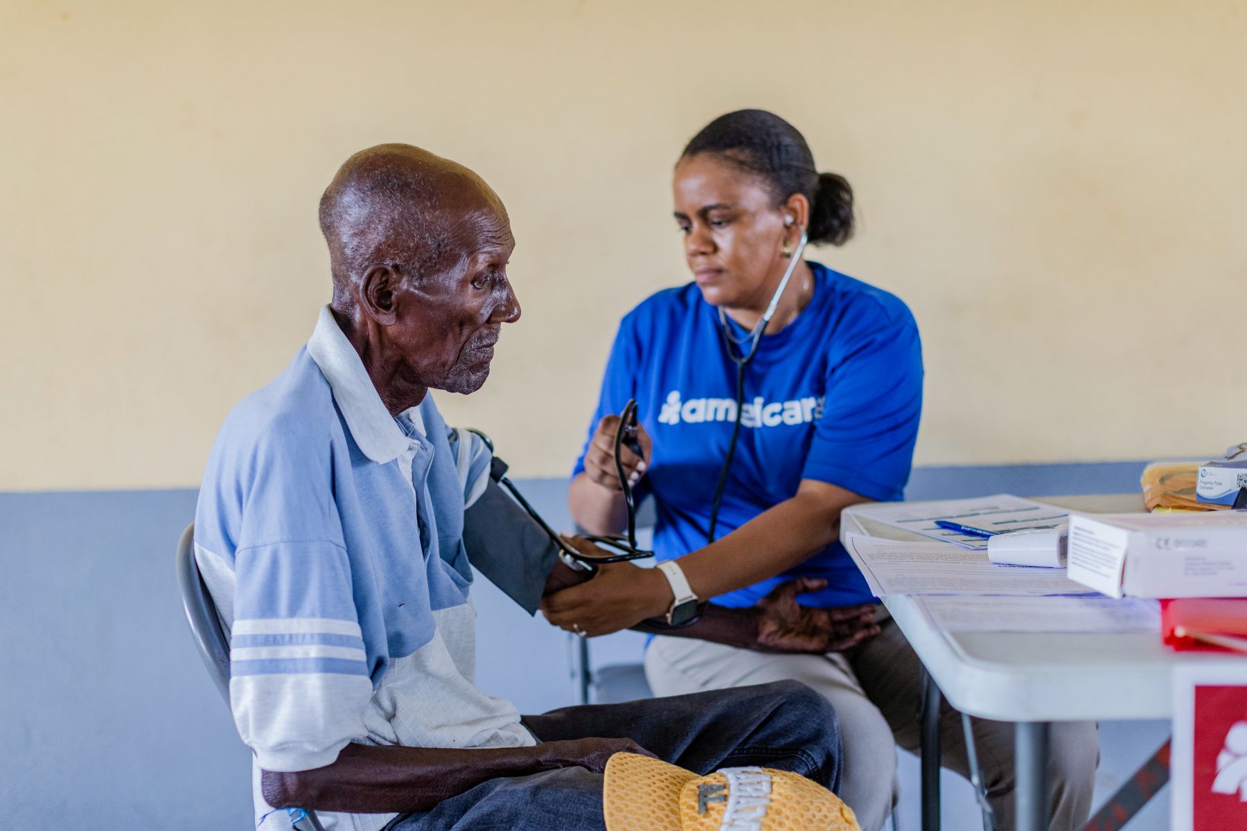 Doctor in blue shirt with stethoscope and blood pressure cuff checks blood pressure of elderly man seated at exam table