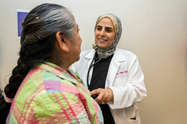 Doctor in white lab coat and hijab with stethoscope examines a patient
