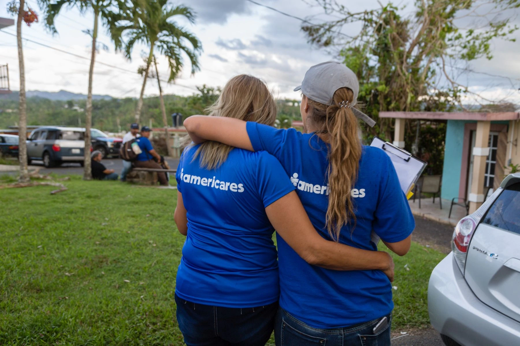 Two women in blue americares shirts have arms around each other as they walk together side by side back to the camera