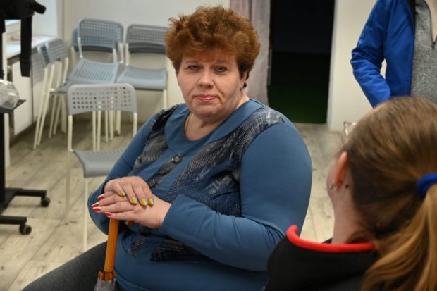 Oksana in a blue top and with her hands on the handle of an umbrella faces a staff member who sits back to the camera.