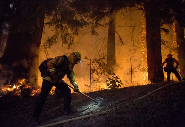 Two CalFire crew digging a fire line with orange flames near by.