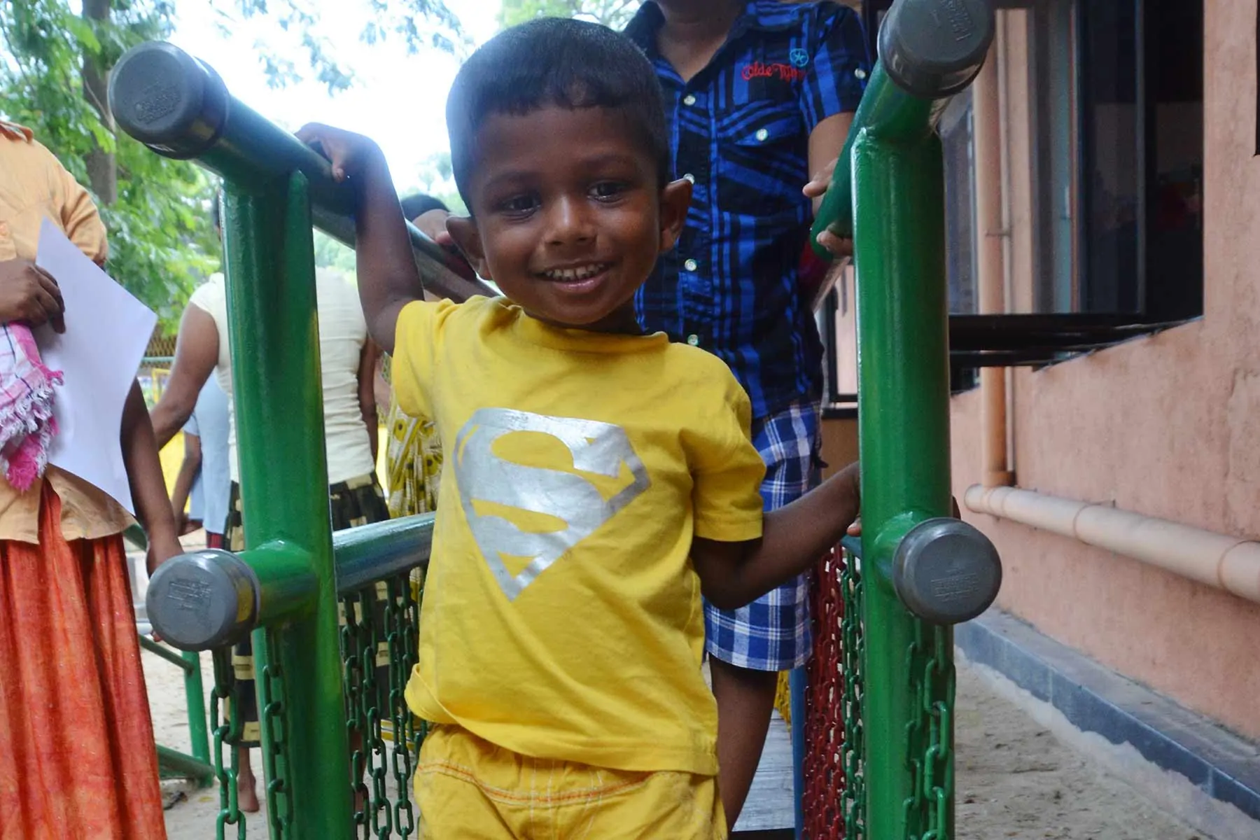Young boy with a superman t-shirt smiles playing outside.